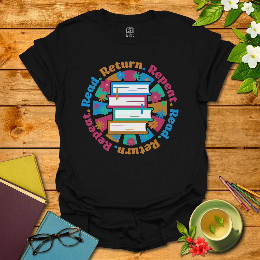 Black unisex T-shirt with a colorful book stack and floral design, encircled by the phrase 'Read. Return. Repeat.' Displayed on a styled background with books and a cup of tea.