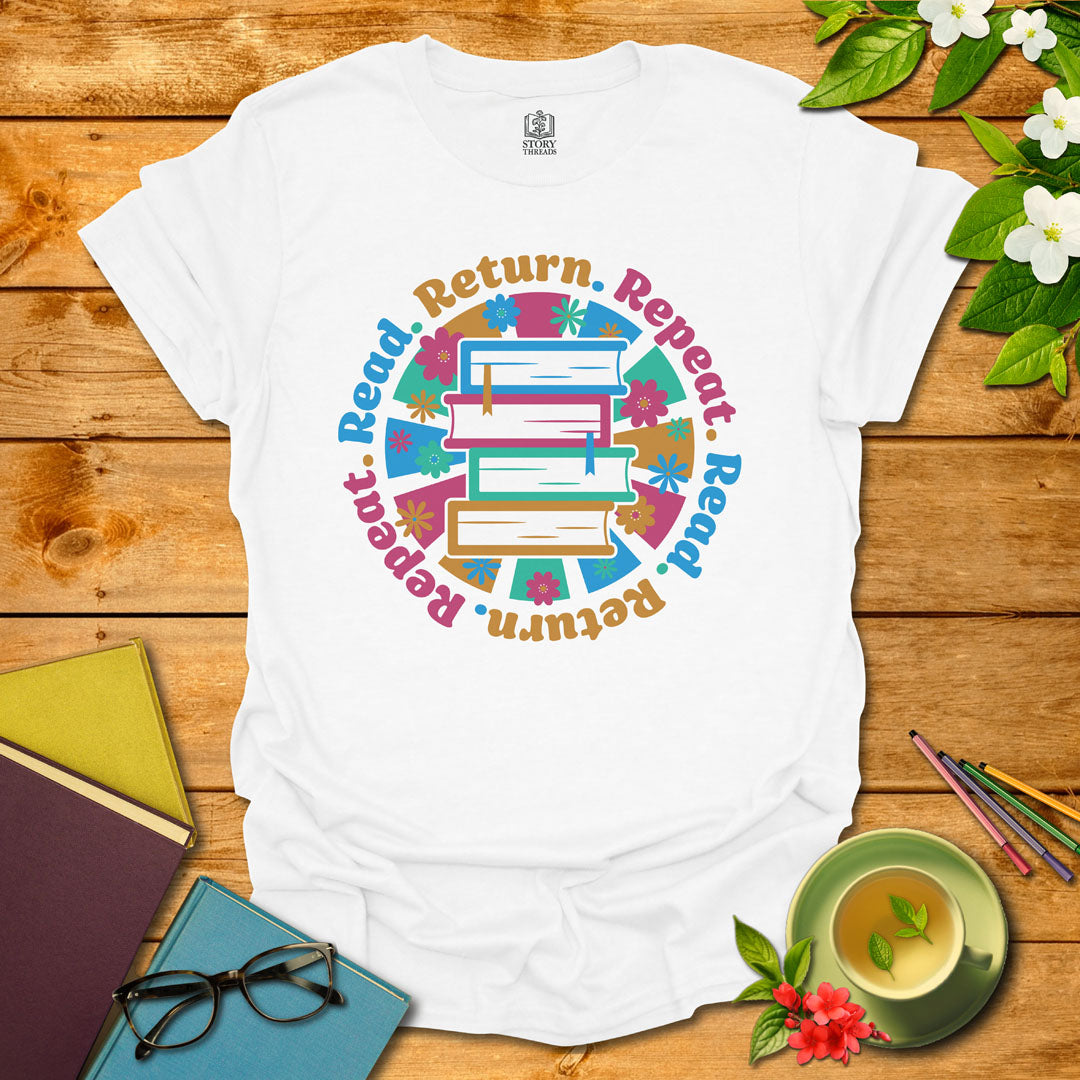 White unisex T-shirt with a colorful book stack and floral design, encircled by the phrase 'Read. Return. Repeat.' Displayed on a styled background with books and a cup of tea.